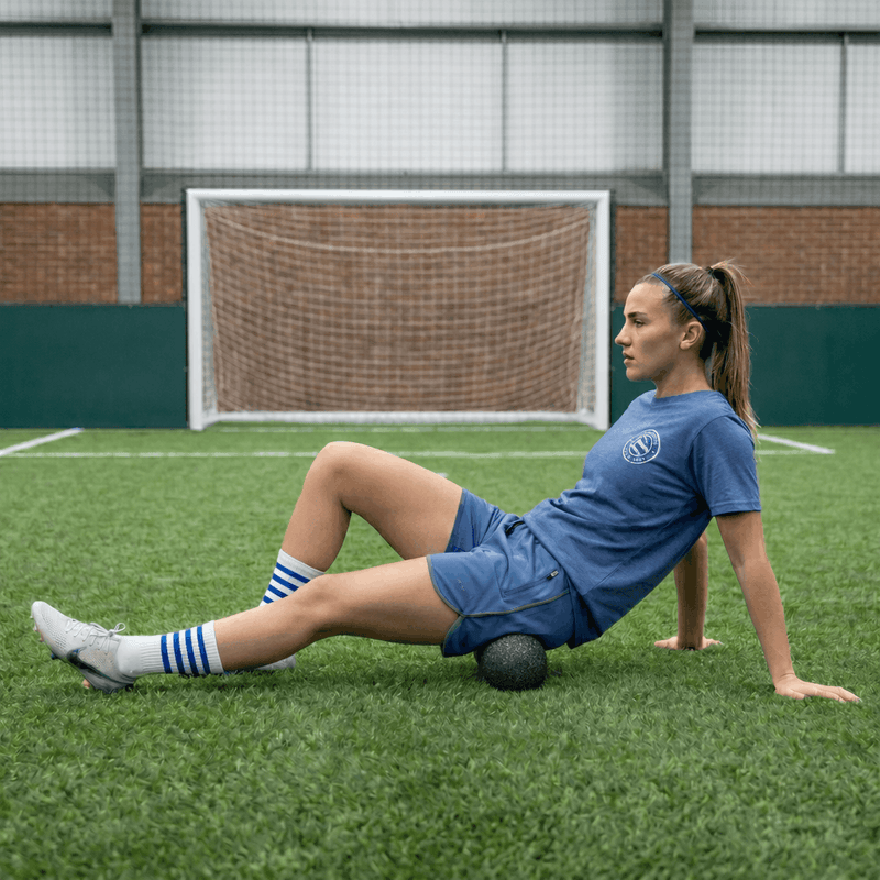 Woman in blue sports uniform stretching on a soccer field with a goal in the background