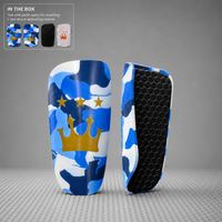 A pair of protective shin guards with a blue, white, and navy camouflage pattern and a gold crown graphic, shown alongside their black honeycomb-textured backing. An inset in the top-left corner displays the included items: two shin pads, a black shock-absorbing insert, and a white nail tip template.