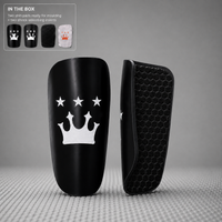 Black shin guard with a white crown and star design, shown alongside its textured black protective insert. Includes a small inset graphic in the top-left corner detailing the included moulding and shock-absorbing inserts.
